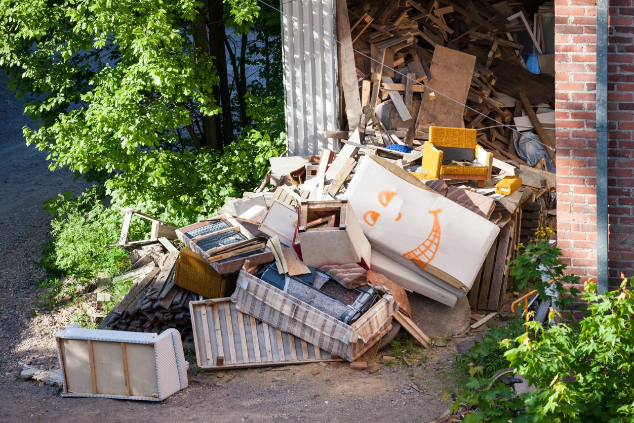 Large pile of discarded furniture, mattresses, and wood debris outside a building